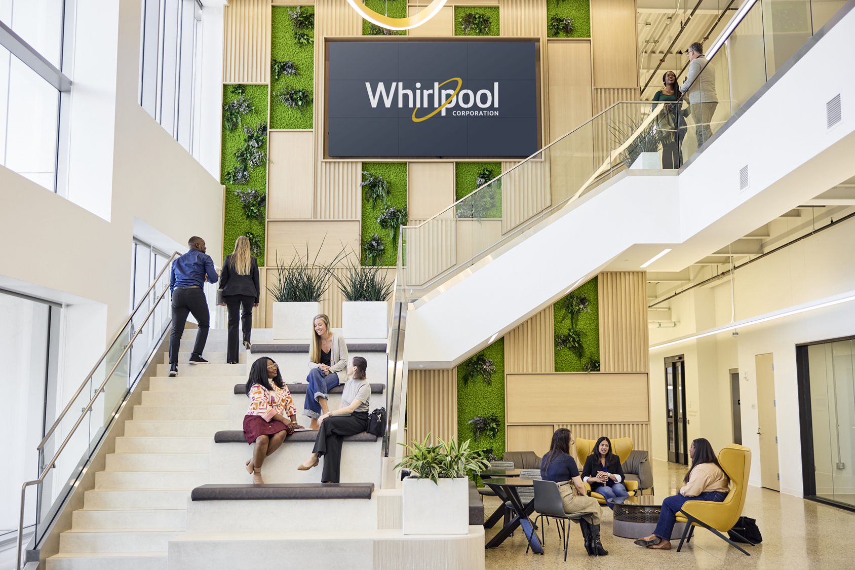 Two coworkers chatting on a balcony at Whirlpool Corporate offices. A pretty African American woman is on the left smiling shyly and a young man is on the right. Photo was taken from the downstairs lobby